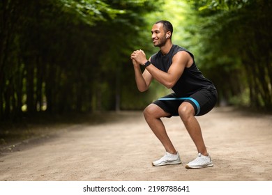 Motivated Handsome Muscular Millennial Black Man Exercising In Public Park, Using Elastic Fitness Band, Enjoying Outdoor Workout, Panorama With Copy Space. Sports Lifestyle And Millennials