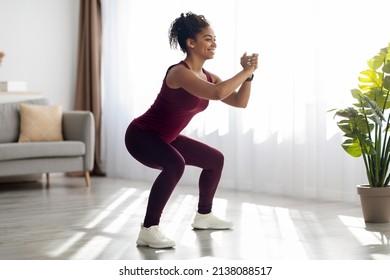 Motivated millennial african american woman in sportswear exercising at living room alone, doing squats, working on buttocks, looking at copy space and smiling, side view. Sport at home - Powered by Shutterstock