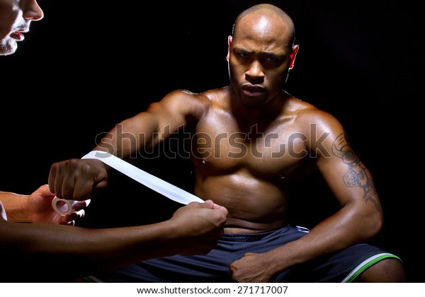 Motivated MMA fighter or Boxer with trainer\
applying athletic tape.  Sitting and lit from above to simulate a\
ringside corner.