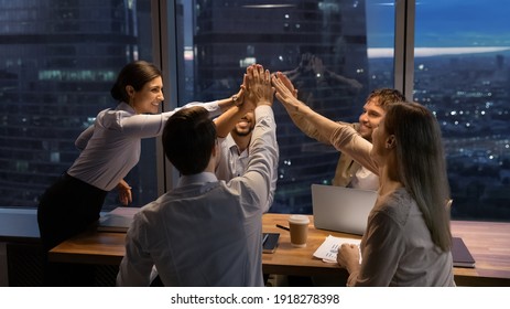 Motivated multinational team raise high fives on briefing after finding problem solution as successful brainstorm result. Happy workers unite hands above conference desk celebrate common achievement
