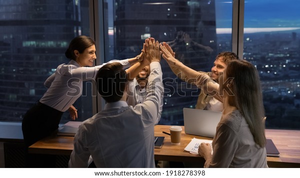 Motivated multinational team raise high fives\
on briefing after finding problem solution as successful brainstorm\
result. Happy workers unite hands above conference desk celebrate\
common achievement