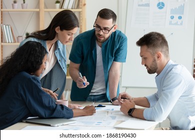 Motivated multiracial diverse businesspeople brainstorm work together on paperwork at team meeting in office. Concentrated young multiethnic colleagues discuss business ideas. Teamwork concept. - Shutterstock ID 1868190430
