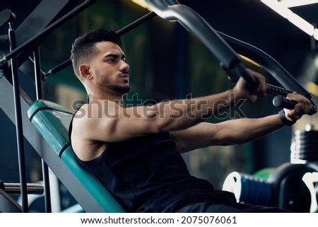Motivated Muscular Arab Man Training On Sport Machine At Gym, Middle Eastern Male Athlete Making Shoulder Press Exercise During Workout In Modern Sport Club, Enjoying Bodybuilding, Closeup Shot