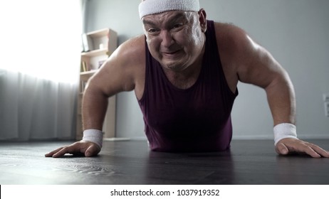 Motivated plump man in his 50s doing push-up with great effort, home training