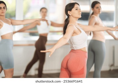 Motivated sporty teenage girl participating in beginner group ballet class, practicing graceful dance movements in sunlit choreography studio - Powered by Shutterstock