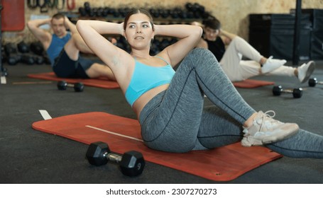 Motivated sporty young woman lying on her back and training core muscles during group training class in CrossFit center