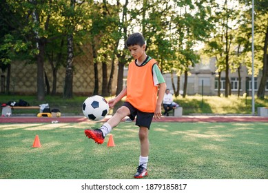 Motivated teen football player stuffs soccer ball on leg. Practicing sport exercises at artificial stadium. - Powered by Shutterstock