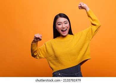 Motivated triumphant girl celebrating victory and feeling optimistic and independent. Positive optimistic woman raising arms while feeling strong and confident on orange background. - Shutterstock ID 2133781979