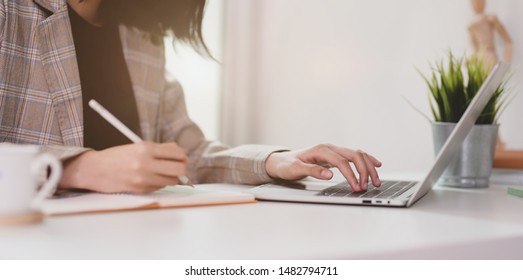 Motivated young businesswoman planing her strategy while typing on laptop and writing on notebook  - Powered by Shutterstock