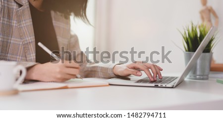 Motivated young businesswoman planing her strategy while typing on laptop and writing on notebook 
