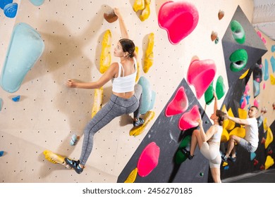 Motivated young girl climbing without ropes and harnesses on artificial bouldering wall in modern fitness center. Active lifestyle and recreation concept.. - Powered by Shutterstock