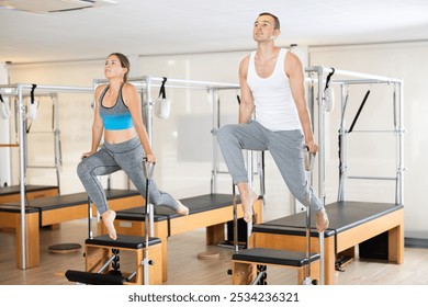 Motivated young man and woman leading healthy, active lifestyle, performing challenging Pilates exercises on Wunda chairs in modern bright studio .. - Powered by Shutterstock