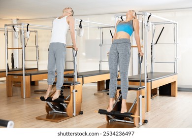 Motivated young man and woman leading healthy, active lifestyle, performing challenging Pilates exercises on Wunda chairs in modern bright studio .. - Powered by Shutterstock