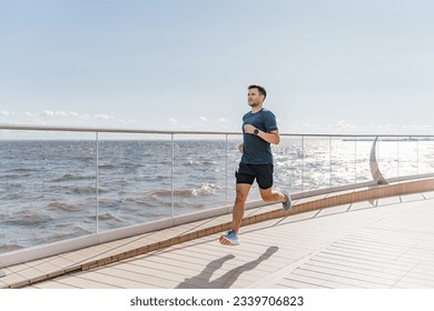 Motivation a male trainer does sports beautifully running. A happy athlete is a person. Using a smartwatch, a runner guy in fitness clothes looks at the time.