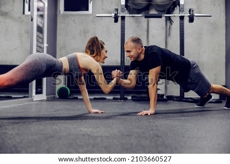 Motivation and support in training, sports lifestyle. The couple does sports exercises together. They are in push ups position and holding hands to maintain body balance. Fitness challenge
