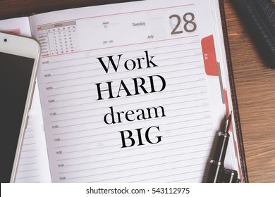 Motivation Text in notepad (diary), which lies on a wooden table with business accessories, mobile phone and fountain pen. Top view with free space.