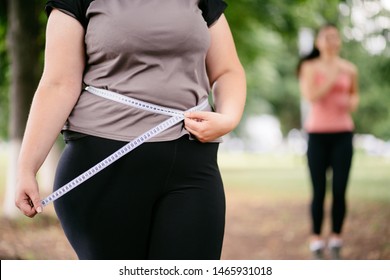 Motivation, Weight Loss, Active Lifestyle, Group Training, Personal Coach. Fat Woman Measuring Her Waistline With Sporty Female Jogger Working Out At Background