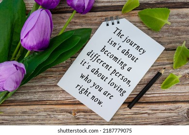 Motivational Quote On Notepad With Flowers On Wooden Desk - The Journey Is Not About Becoming A Different Person, It Is About Loving Who You Are Right Now.