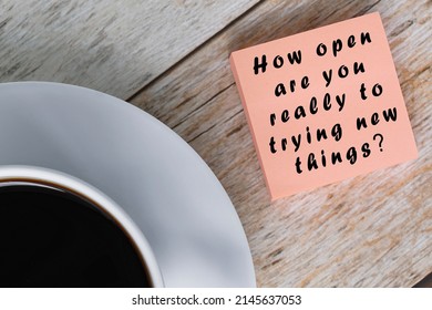 Motivational Quote On Notepad With White Coffee Cup On Wooden Desk - How Open Are You Really To Trying New Things. Questions.