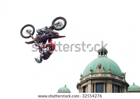 Motocross biker performing dangerous trick - back flip next to cupola of old stylish building isolated on white