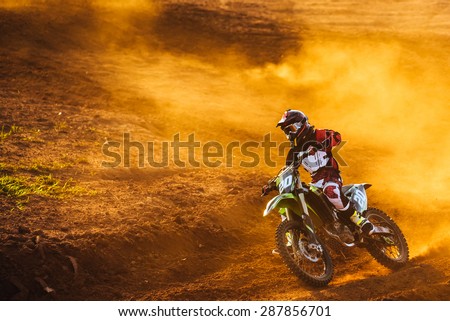 Motocross pilot in a turn during sunset with golden smoke on dirt track