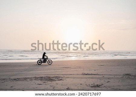 Motocross rider driving along the beach at sunset