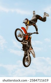 Motocross rider performs acrobatic stunt on dirt bike in mid air against bright blue sky, showcasing extreme sports skills, balance and adrenaline action. Extreme sport and freestyle motocross concept