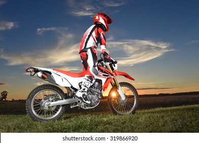Motocross rider standing on motocycle during sunset 