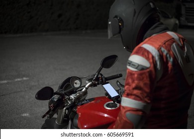 Motor Bike Driver With Smartphone Mobile Phone On A Motorcycle With Helmet In The Night