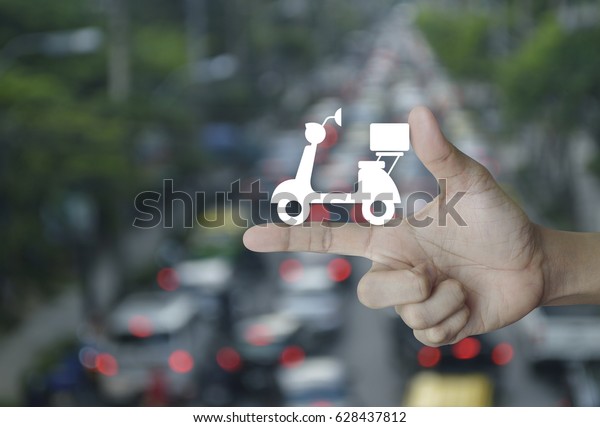 Motor bike icon on\
finger over blur of rush hour with cars and road, Business delivery\
service concept