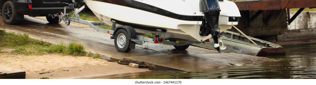 Motor boat launch, white vessel on trailer roll on concrete shipway to water