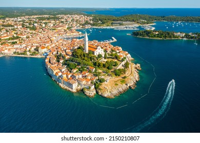 The motor boat sailing around Rovinj. Surroundings of Rovinj and tower of St. Euphemia church. Croatian town buildings near forests and Adrianic sea at bright sunlight. Aerial panorama