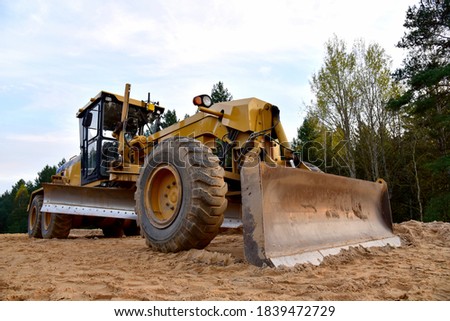 Motor Grader on road construction in forest area. Greyder leveling the sand, ground and gravel during road work. Heavy machinery and construction equipment for grading. Earthworks grader machine