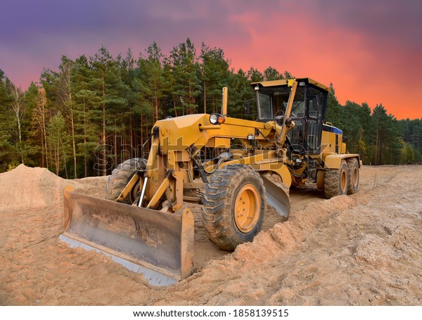 Motor Grader on road construction in forest area.\
Greyder leveling the sand, ground and gravel during road work.\
Heavy machinery and construction equipment for grading. Earthworks\
grader machine