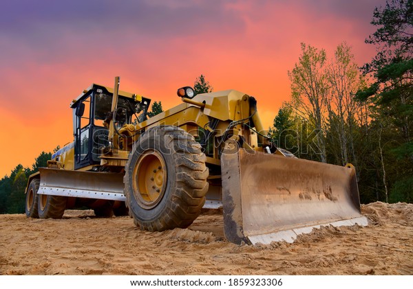 Motor Grader on road construction in forest area.\
Greyder leveling the sand, ground and gravel during road work.\
Heavy machinery and construction equipment for grading. Earthworks\
grader machine