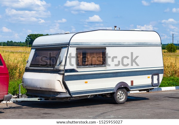 A motor home in the form of a\
white trailer in a parking lot near the road, secured to the car\
while traveling in remote uninhabited places. Movable\
property.