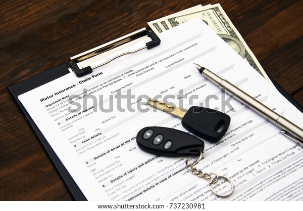 Motor insurance claim form, car key and pen on\
wooden desc