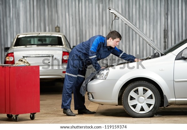 motor mechanic diagnosing\
automobile car engine before maintenance at repair service\
station