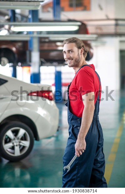 Motor service. Smiling bearded man with\
wrench walking to car at auto service\
station