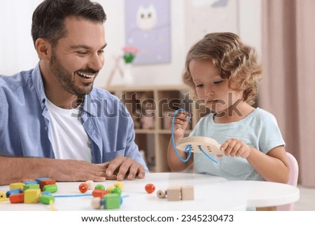 Motor skills development. Father and daughter playing with wooden lacing toy at table indoors