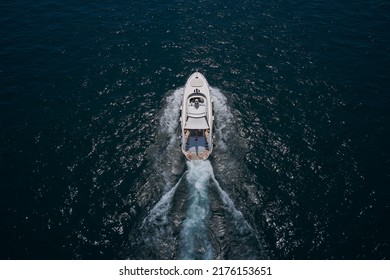 Motor Yacht In Motion Top View, Back. White Yacht On The Sea Aerial View. Superyacht Is Moving Fast On The Water Top View. A Huge Super Mega Yacht In White On Dark Blue Water In Italy.