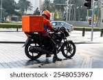 Motorbike delivery man wearing orange uniform and ready to send food. Delivering Food. Delivery man of take away with isothermal food pink case box driving find home. Express food delivery service.