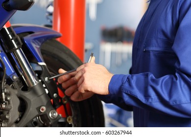 Motorbike mechanic hands disassembling parts in a workshop with equipment in the background - Powered by Shutterstock