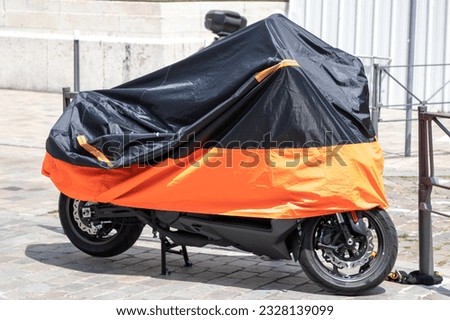 motorbike orange black protected by plastic cover in street motorcycle with tarpaulin jacket