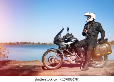 Motorbiker travelling, autumn day, motorcycle off road, rider, adventurer, extreme tourism, cold weather clothes, near the lake, light tinting, uses smartphone, internet, search, - Powered by Shutterstock