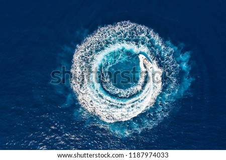 Motorboat forms a circle of waves and bubbles with its engines over the blue sea