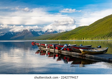 Motorboats lined up on a dock reflected in a beautiful lake with snow-capped mountains in the background at Lake McDonald in Glacier National Park - Powered by Shutterstock