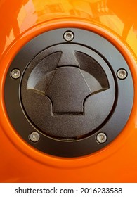 Motorcycle Or Airplane Fuel Tank Cap. In Black Color With Aluminum Screws Attached To The Orange Bodywork.