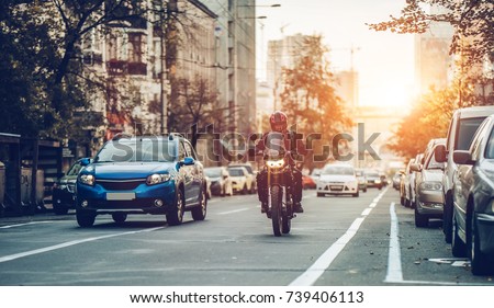 Motorcycle and cars are riding on street. City during the sunset.