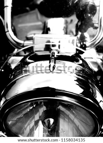 Motorcycle chrome front light, front closeup of motorcycle light and screen visor in monochrome and black and white. Chrome light reflection and glass bulb.